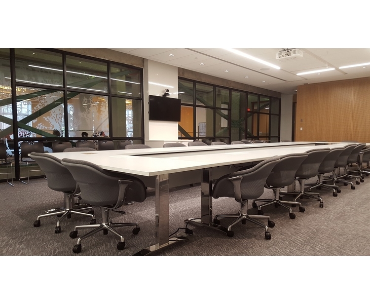 Large modern-looking room with with long narrow conference table in the center and gray wheeled armchairs around its perimeter